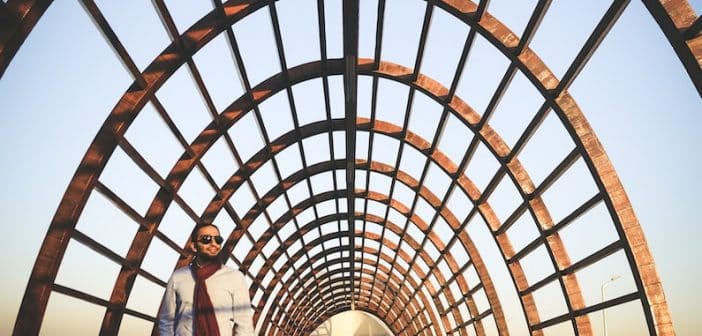 man and woman standing on brown wooden pathway under brown metal arch